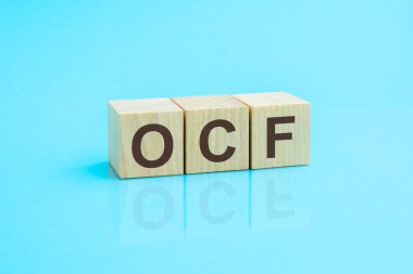 ocf - ahşap blokların kısaltması mavi arkaplanda harflerle. Tablonun aynalı yüzeyindeki başlığın yansıması. Seçici odaklanma. ocf - nakit akışının kısaltılmışı