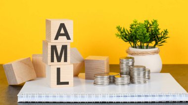Masada AML metni olan tahta küp. Sarı arka plan. Bozuk paraları beyaz not defterine istifleyin. finansal, pazarlama ve iş kavramları
