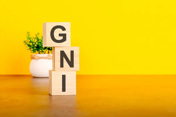 stock image Three wooden cubes with letters - GNI on yellow table, space for text in right. front view concepts, flower in the background. GNI - short for Gross national income