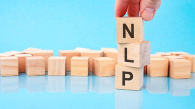 Genç bir iş adamının, ahşap bir küple ahşap bir arkaplanda mavi bir arkaplan üzerinde N. N. NLP harfini tutarken görüntüsünü kapat.
