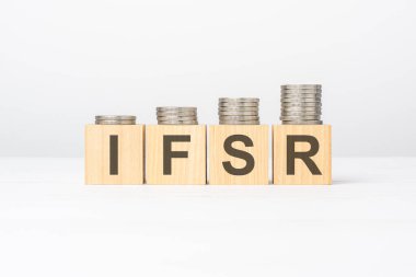 Tahta blokta yazılı IFSR metni beyaz arka planda yığılı paralar, iş konsepti. IFSR - Sigorta Finansal Güç Beğeni 'nin kısaltması