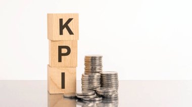 kpi - beyaz arkaplandaki tahta küplerin üzerinde bozuk paralarla birlikte metin