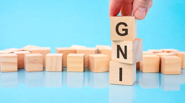 stock image close up image hand of a young businessman holding a wooden cube with letter G. GNI on wooden cube on a blue background with copy space