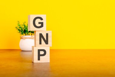 İçinde harfler olan üç tahta küp. Sarı masada GSMH, sağda yazı için boşluk. Ön görüş kavramları, arka planda çiçekler. GSMH - kısaltma brüt ulusal ürün