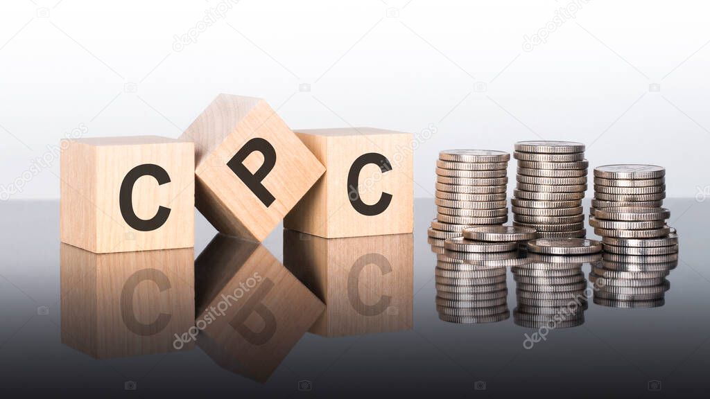 cpc - text is made up of letters on wooden cubes lying on a mirror surface, gray background. stacks with coins. inscription is reflected from the surface. CPC - short for Cost Per Click