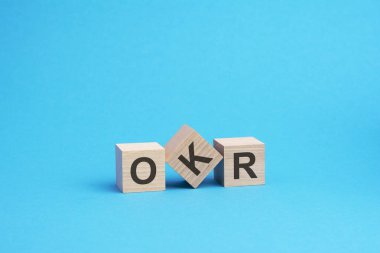 Tahta bloklar üzerine OKR metni, finansal iş konsepti, mavi arka plan. OKR - Hedefler ve Anahtar Sonuçların kısaltması
