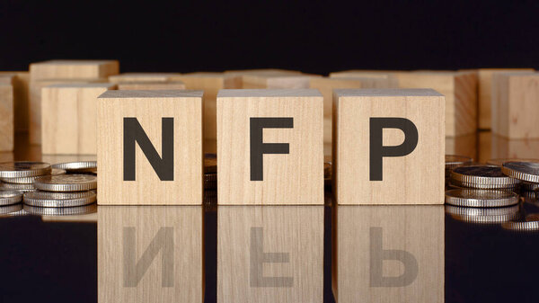 NFP - сокращение от Non-Farm Payroll. текст на деревянных кубиках с монетами, черный фон, бизнес-концепция. Надпись на кубиках отражается с поверхности черного стола. вид спереди