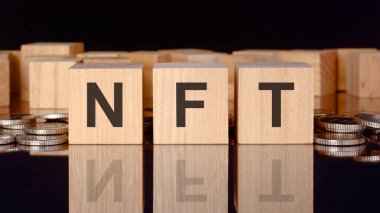 NFT - Finansal olmayan jetonun kısaltılmışı. Bozuk paralar, siyah arka plan ve iş konsepti içeren tahta küplerle ilgili yazı. Küplerdeki yazıtlar siyah tablonun yüzeyinden yansıyor. ön görünüm