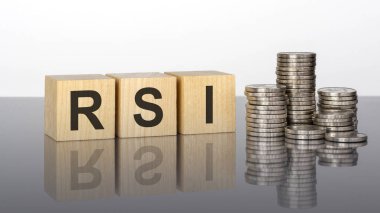 RSI - metin, ayna yüzeyinde duran tahta küplerdeki harflerden oluşur, gri arkaplan. Bozuk paralarla dolu desteler. Yazı yüzeyden yansıtılır. RSI - Göreceli Kuvvet İndeksinin kısaltması