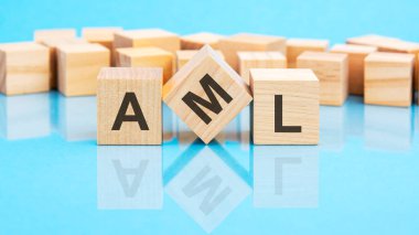 Tahta küplere siyah harflerle yazılmış AML yazıları. Küpler parlak mavi cam bir yüzey üzerinde yer alıyor. konsept kelime arka planda küplerle şekilleniyor. AML - Para Aklamayla Mücadele 'nin kısaltması