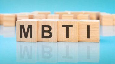 Mavi arka planda ahşap küplerde MBTI kelimesi. Küplerdeki yazılar yüzeyden yansıyor. İş konsepti. MBTI - Myers-Briggs Tip Göstergesinin kısaltması