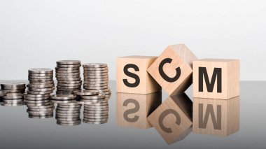 scm - metin, ayna yüzeyinde duran tahta küplerdeki harflerden oluşur, gri arkaplan. Bozuk paralarla dolu desteler. Yazı yüzeyden yansıtılır. scm - Tedarik Zinciri Yönetiminin kısaltması