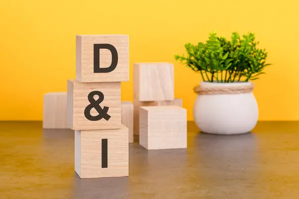 Three wooden cubes with letters - D and I on yellow table, space for text in right. front view concepts, flower in the background. DI - Diversity and Inclusion acronym