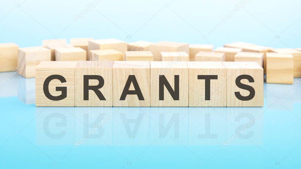 word grants made with wood building blocks. text is written in black letters and is reflected in the mirror surface of the table, blue background, business concept