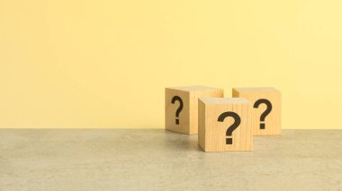 Gri taş masa üzerinde soru işaretleri olan tahta küpleri, yakın plan. Mesaj için yer var. sarı arkaplan,