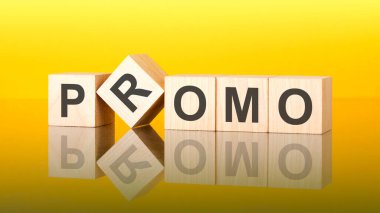 Tahta blokta yazan tanıtım kelimesi. Sarı arka plan. İş konsepti. Küplerdeki yazıtlar masanın yüzeyinden yansıyor. bir renk gradyanı kullanılıyor
