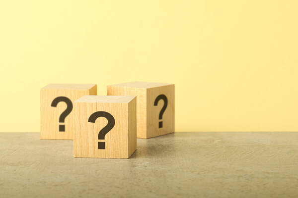Wooden cubes with question marks on grey stone table, closeup. Space for text. yellow background,