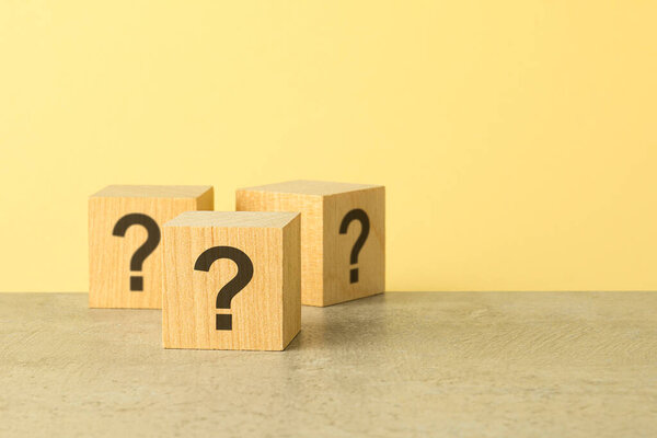 wooden cubes with question marks on grey stone table, closeup. space for text. yellow background