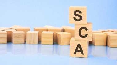 Parlak mavi bir arka planda, tahta bloklar ve metinli küpler. Küpler yüzeyden yansıyor. sca - güçlü müşteri kimlik denetiminin kısaltması