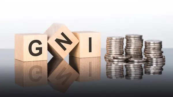 stock image gni - text is made up of letters on wooden cubes lying on a mirror surface, gray background. stacks with coins. inscription is reflected from the surface. gni - short for Gross national income