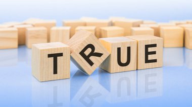 Mavi bir masanın parlak yüzeyinde dört tahta blok ve gerçek harf var. Küplerdeki yazıt yüzeyden yansıyor.