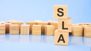 SLA. Tahta küpler. Siyah arka planda bloklar var. Bozuk paralarla dolu desteler. Küplerdeki yazıtlar masanın yüzeyinden yansıyor. Seçici odaklanma. SLA - Hizmet Seviyesi Anlaşması 'nın kısaltması.