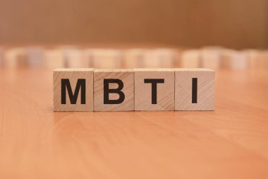 Mavi bir masanın parlak yüzeyinde üzerinde MBTI harfleri olan dört tahta blok. Küplerdeki yazılar yüzeyden yansıyor. MBTI - Myers-Briggs Tip Göstergesi.