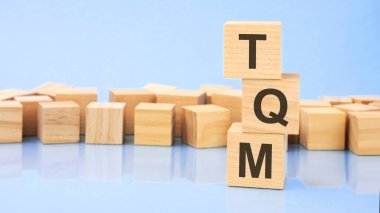 TQM. Tahta küpler. Siyah arka planda bloklar var. Bozuk paralarla dolu desteler. Küplerdeki yazıtlar masanın yüzeyinden yansıyor. Seçici odaklanma. TQM - Toplam Kalite Yönetiminin kısaltması