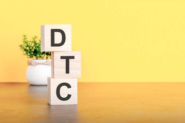 İçinde harfler olan üç tahta küp. Sarı masada DTC, sağda yazı için yer var. Ön görüş kavramları, arka planda çiçekler. dtc - Doğrudan Tüketiciye 'nin kısaltması