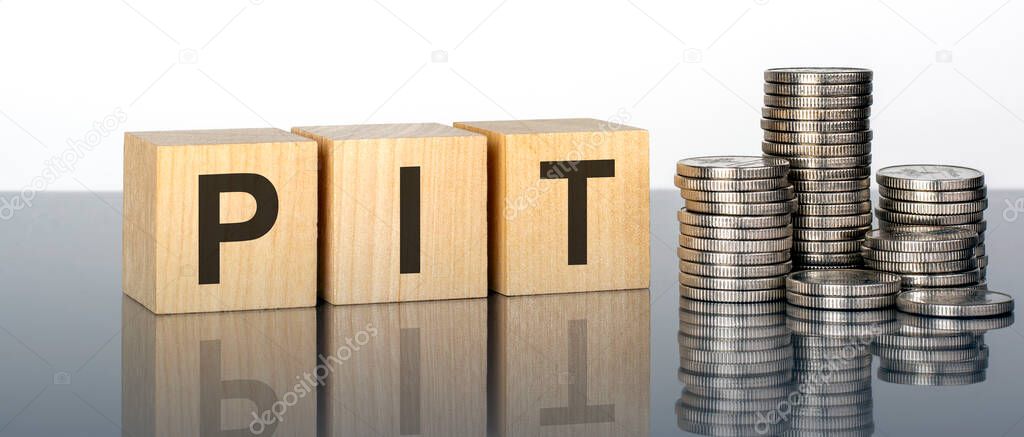 PIT - text is made up of letters on wooden cubes lying on a mirror surface, white background. stacks with coins. inscription is reflected from the surface. pit - short for personal income tax