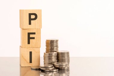 PFI yazılı tahta bloklar. Yüzeyden yansıyan küpler ve paralar. PFI - Özel Finans Girişimi 'nin kısaltması
