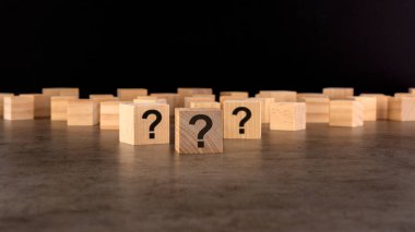 Pek çok tahta küpün önünde soru işaretleri var. Birçok soru ortaya çıkıyor. Sorun ve karışıklık. siyah arkaplan.