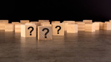 Pek çok tahta küpün önünde soru işaretleri var. Birçok soru ortaya çıkıyor. Sorun ve karışıklık. siyah arkaplan.