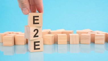 E2E-Exchange to Exchange ile el ele tutuşan tahta küp bloğu. Küplerdeki yazılar yüzeyden yansıyor. Kopyalama alanı olan mavi arkaplan