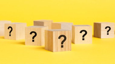 Pek çok tahta küpün önünde soru işaretleri var. Birçok soru ortaya çıkıyor. Sorun ve karışıklık. sarı arkaplan