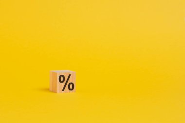 Bir tarafında yüzde işareti olan ahşap bir zar, yakın planda sarı arkaplanda gölge ve kopyalama alanı ile birlikte görülüyor.