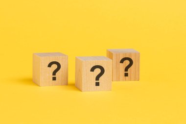 Sarı masada soru işareti olan üç tahta blok, yakın plan. Metin için boşluk. Sarı arka plan. seçici odak