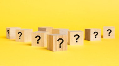 Pek çok tahta küpün önünde soru işaretleri var. Birçok soru ortaya çıkıyor. Sorun ve karışıklık. sarı arkaplan