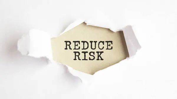 the word REDUCE RISK appearing behind torn white paper, gray background.