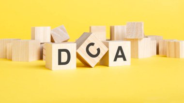 Sarı arka planda DCA yazılı tahta bloklar. Dolar Maliyeti Ortalaması konsepti