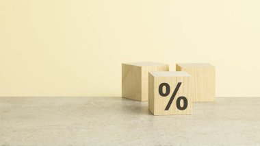 Bir tarafında yüzde işareti olan bir tahta zar, yakın planda, sarı arkaplanda kopya alanı olan bir gölgeyle görülüyor..