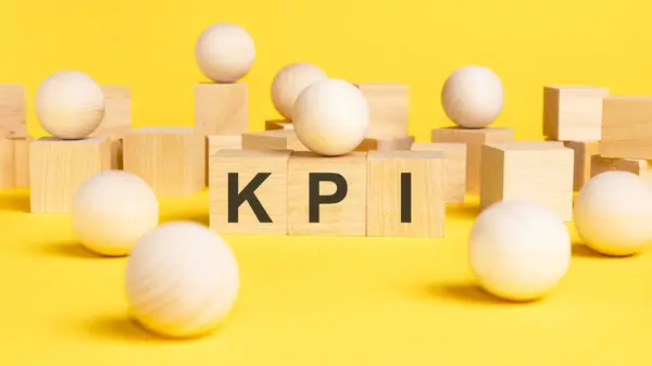 the text KPI is written on wooden cubes on a bright yellow surface. wooden sphere balls among the wood cubes, different and position in niche market concept