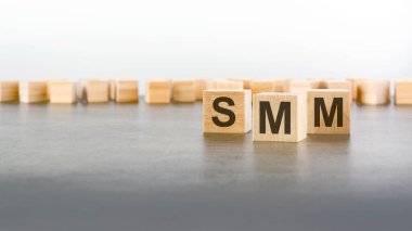 Gri arkaplandaki tahta küplere SMM yaz. 'Sosyal Medya Pazarlaması' nın kısaltması. Kare tahta bloklar. en üstteki görünüm..