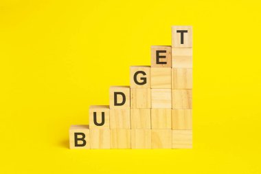 Bütçe kelimesi tahta küp piramidinin üzerine yazılmıştır. Parlak sarı arkaplan üzerindeki bloklar