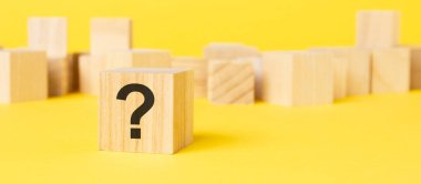 Doğal ahşap blok, üzerinde büyük siyah soru işareti olan bir yüz, sarı arka plan..