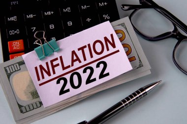 INFLATION 2022 - banknotlara sabitlenmiş beyaz bir kağıt parçası üzerinde kelime bir hesap makinesi, gözlük ve kalem. İş ve finans kavramı