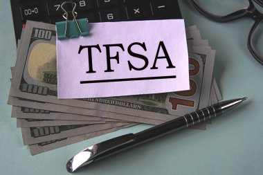 TFSA (Tax Free Savings Account) - acronym on a white piece of paper fixed on banknotes against the background of a calculator, glasses and pen. Business and finance concept