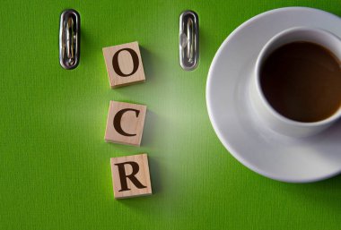 OCR (Optical Character Recognition) - acronym on wooden cubes against the background of a green folder and a cup of coffee. Business and AGI adjusted gross income concept.