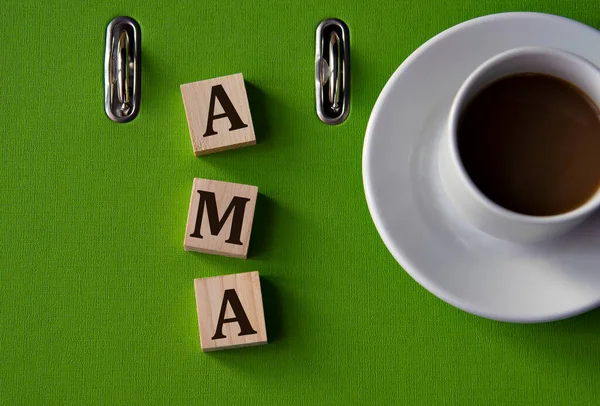AMA (Ask me anything) - acronym on wooden cubes against the background of a green folder and a cup of coffee.