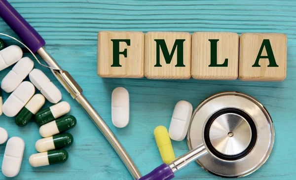 FMLA (Family and Medical Leave Act) - acronym on wooden cubes on a blue background with a stethoscope and tablets. Medical concept